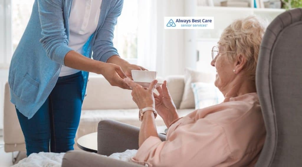 Caregiver handing a cup of tea to a senior woman in a cozy living room, highlighting compassionate care and support for daily living activities.