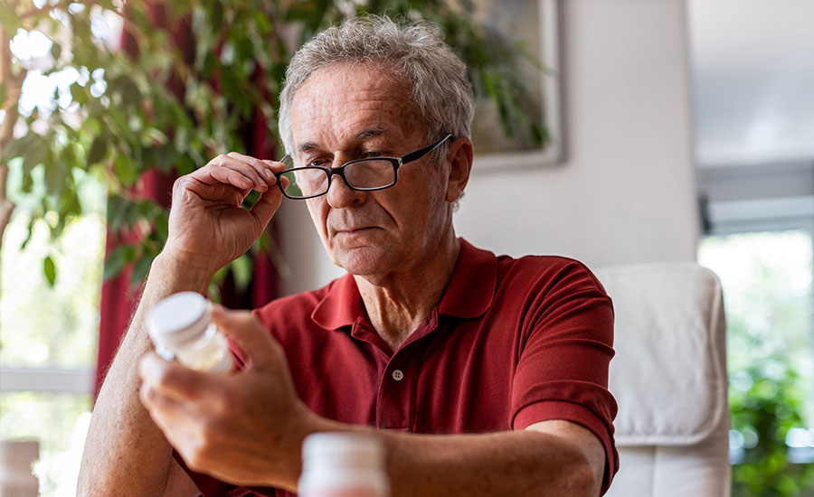 An elderly man looking at a bottle of medications