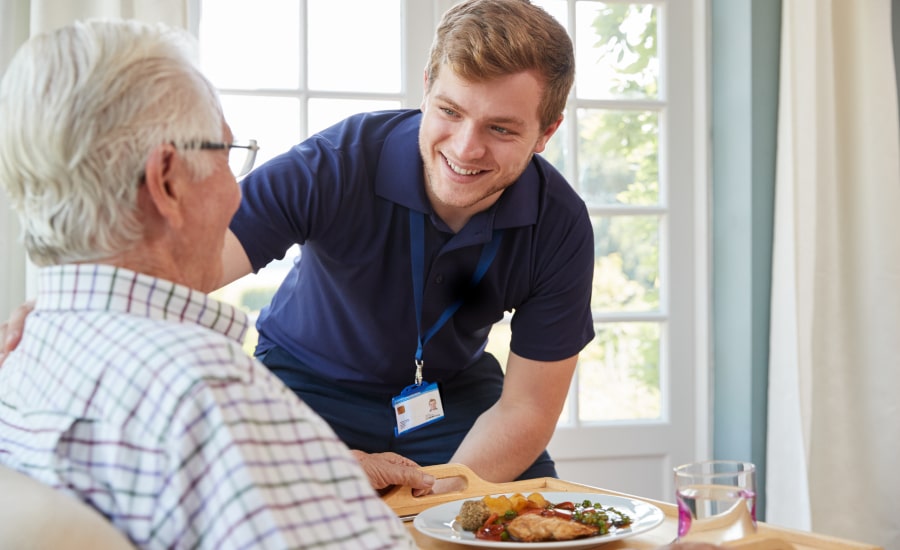 A caregiver preparing a meal for an elderly male​