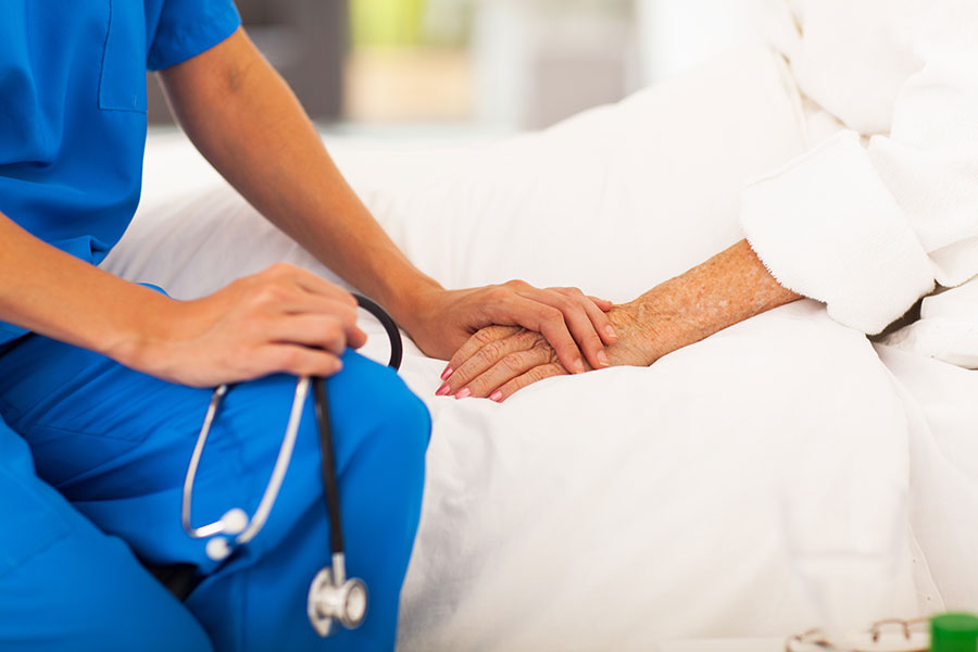 A professional caregiver holding an elderly patient's hand​