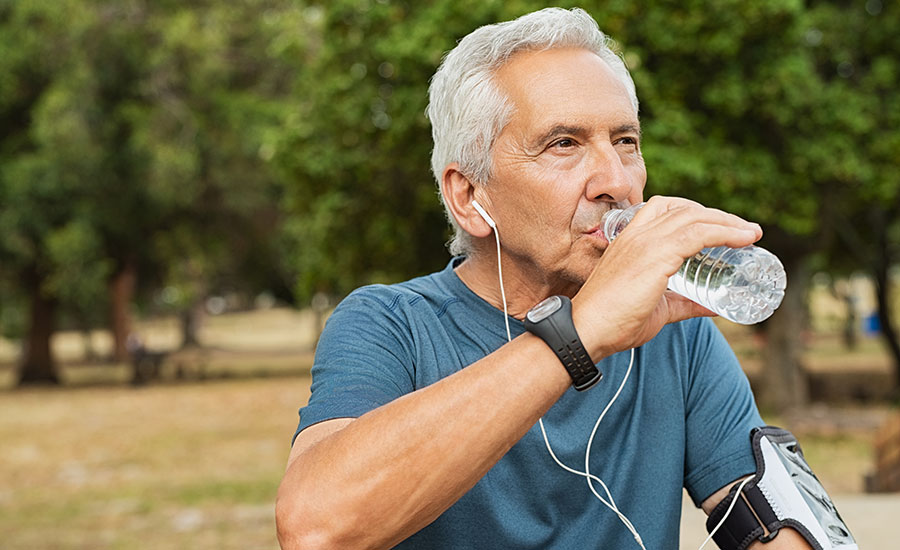 A senior male drinking a bottle of water while exercising​