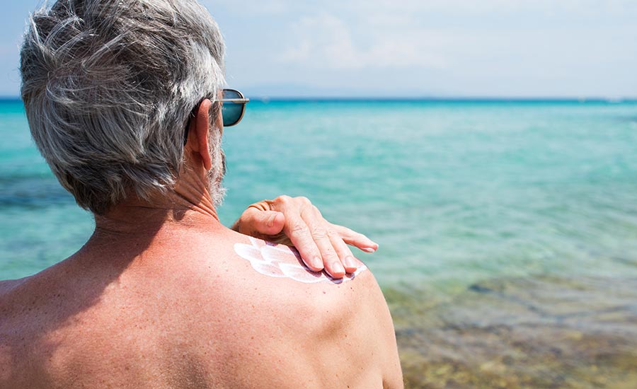 An elderly man applying sunscreen to his skin​