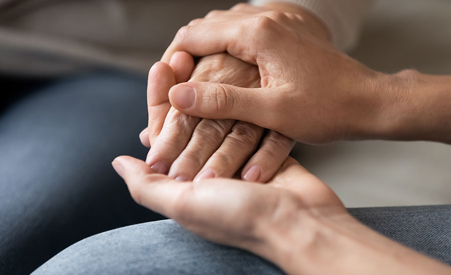 A family caregiver holding their elderly loved one's hand