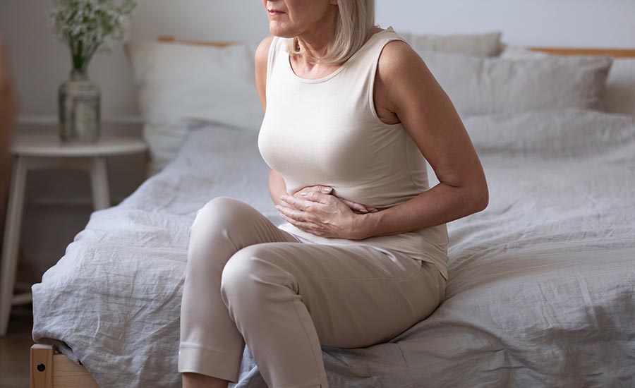 An elderly woman sitting on the bed while holding her stomach​