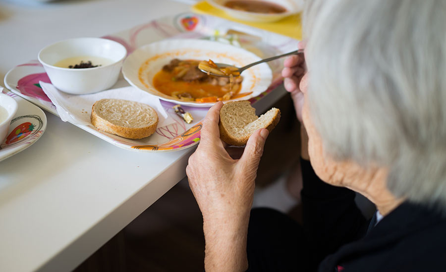 An elderly woman eating a bowl of soup​