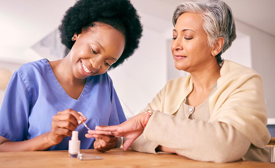 A caregiver applying nail protection on an elderly woman’s nails