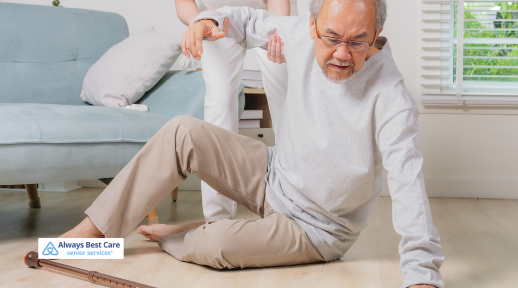 5.  Older man sitting on the floor after a fall with a caregiver reaching to help, emphasizing fall risk and responsive in-home care from Always Best Care.

